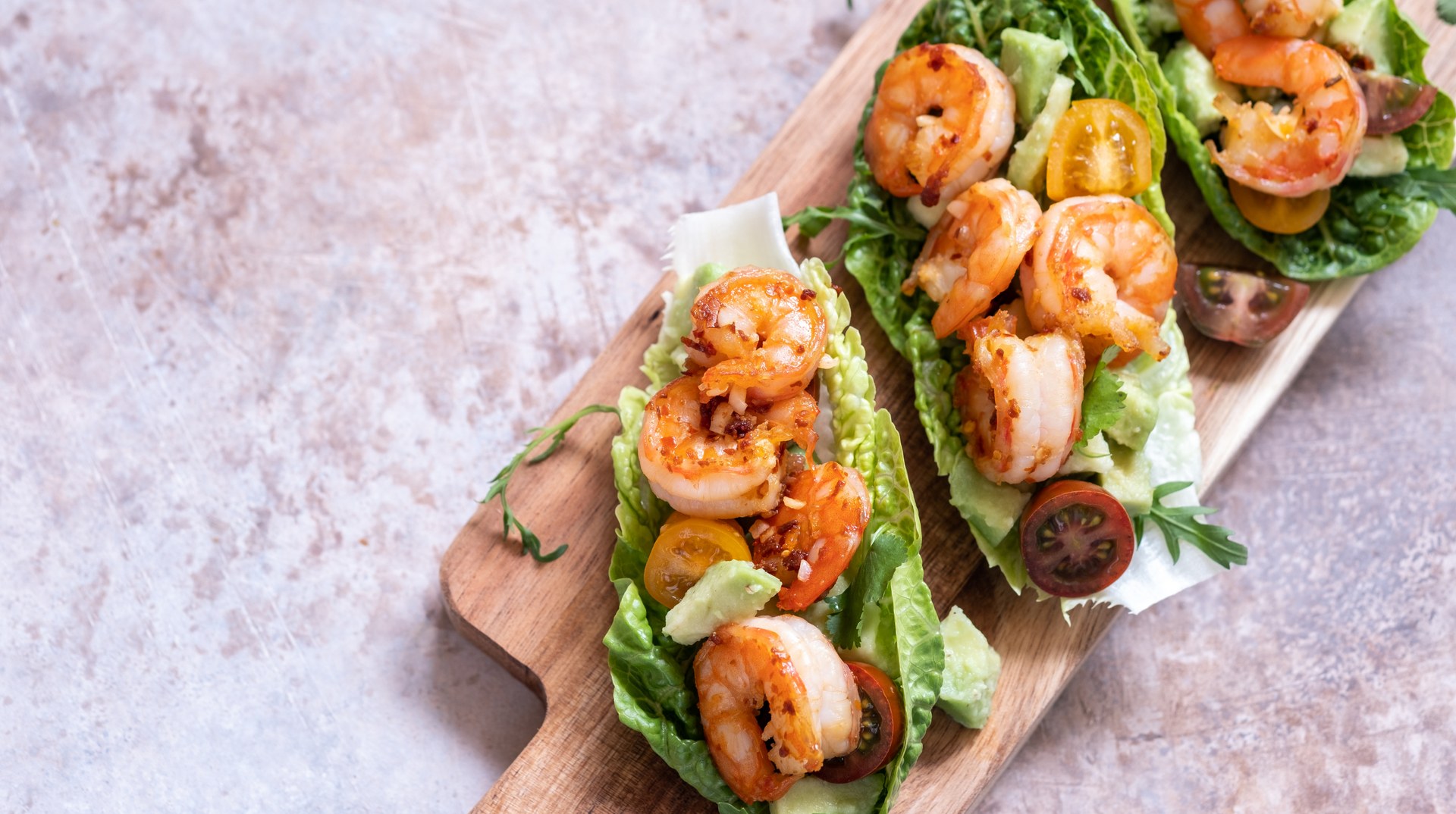 A wooden cutting board topped with shrimp , lettuce , tomatoes and avocado.