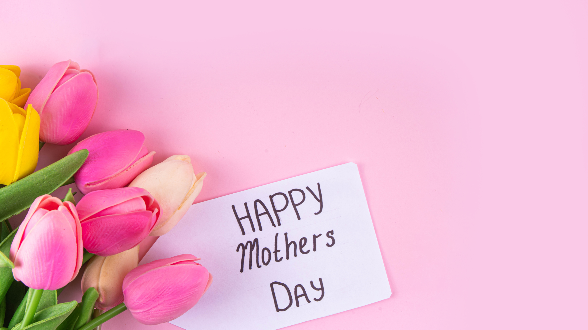 A bouquet of pink and yellow tulips and a happy mother 's day card on a pink background.