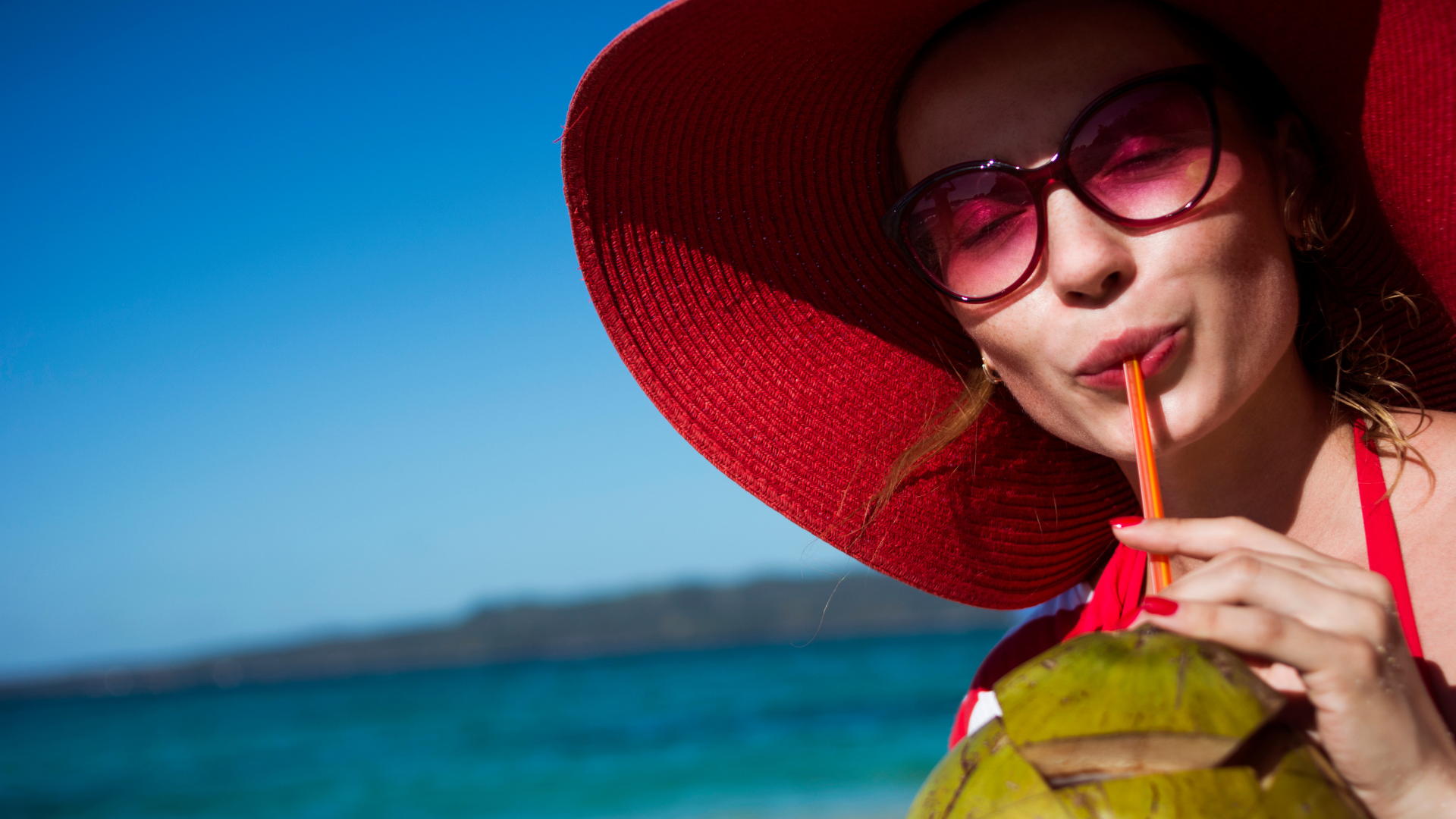 A woman is drinking coconut water through a straw on the beach.