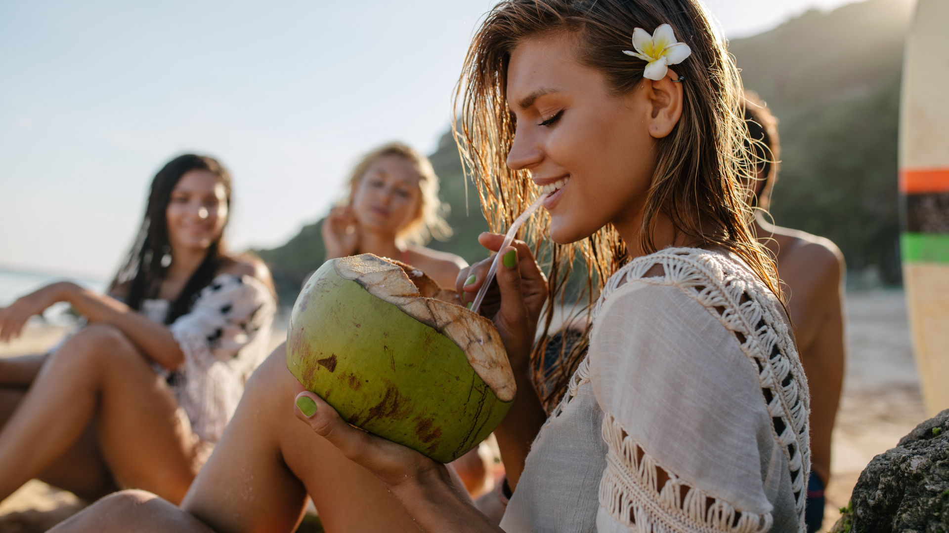 A woman is drinking coconut water from a coconut on the beach.