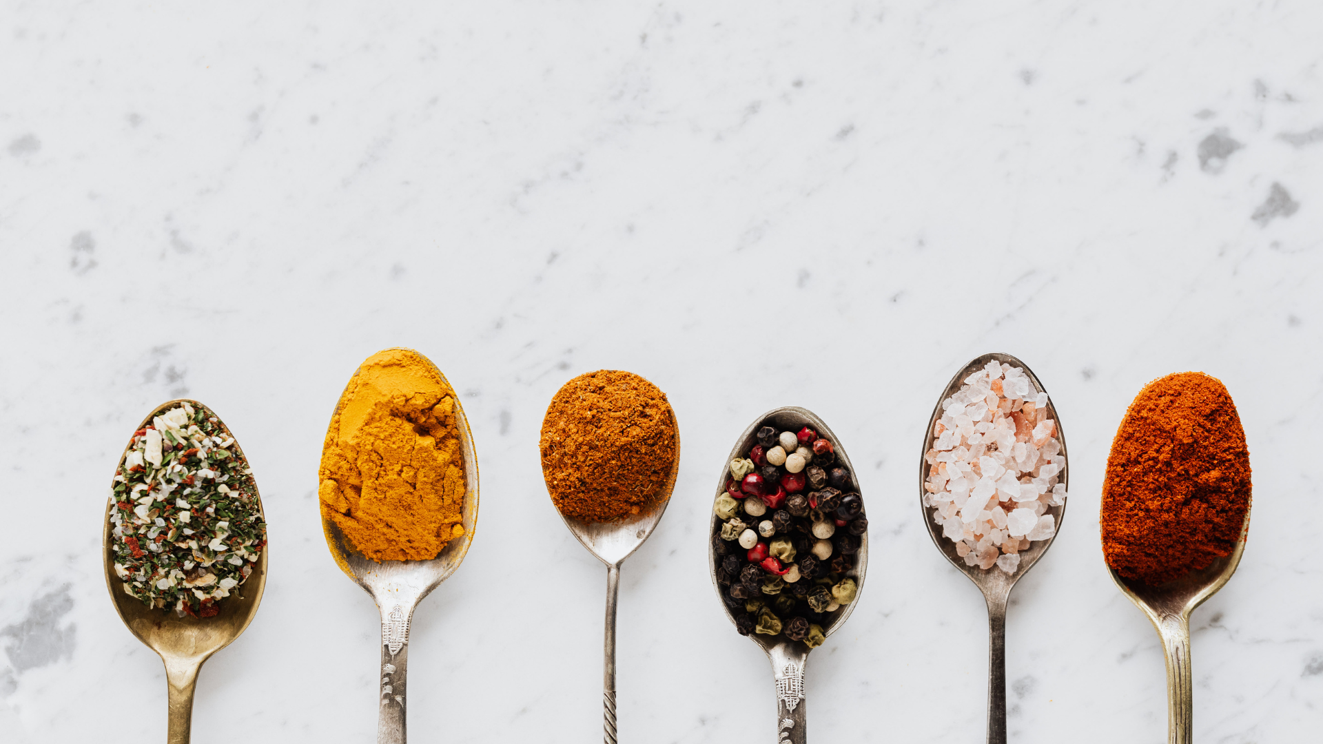 A row of spoons filled with different types of spices.