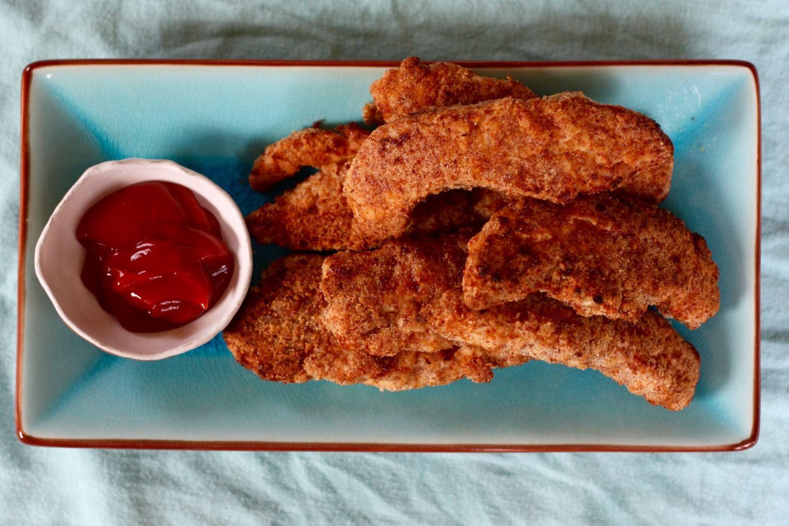 A blue plate topped with chicken nuggets and ketchup.