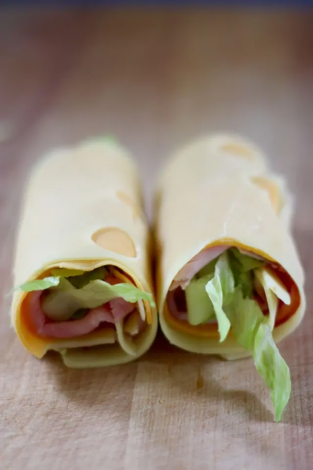 Two wraps with ham and lettuce are sitting on a wooden table.