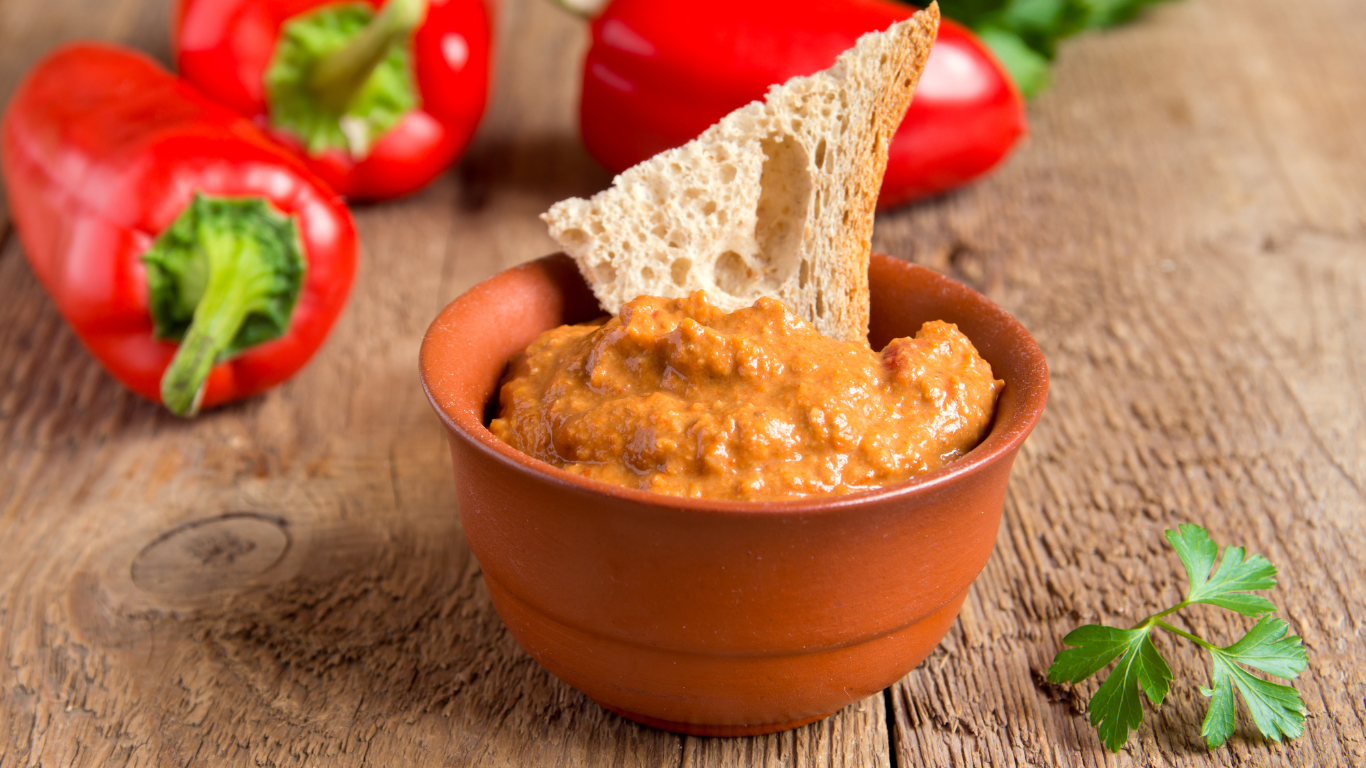 A bowl of dip with a piece of bread sticking out of it on a wooden table.