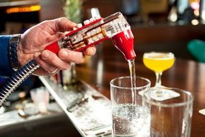 A bartender is pouring a drink into a glass at a bar.