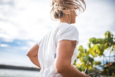 A woman wearing headphones is running on a beach.