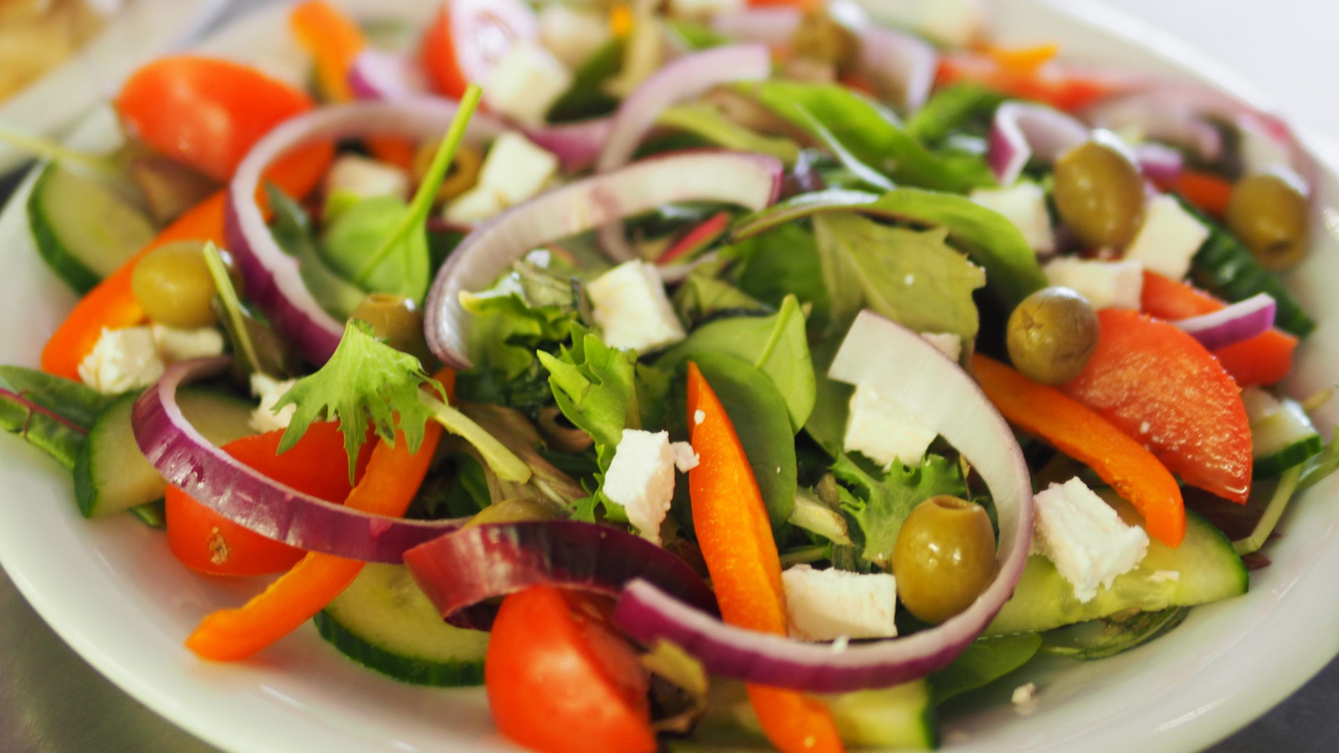 A close up of a salad with tomatoes , cucumbers , onions and olives on a plate.