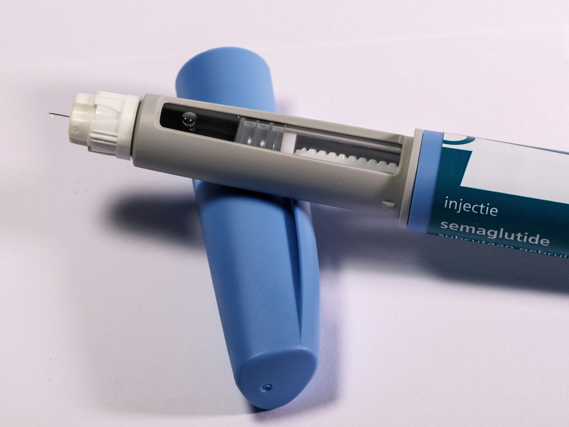 Blue and grey semaglutide injection pen with needle cap removed, lying on a white surface.