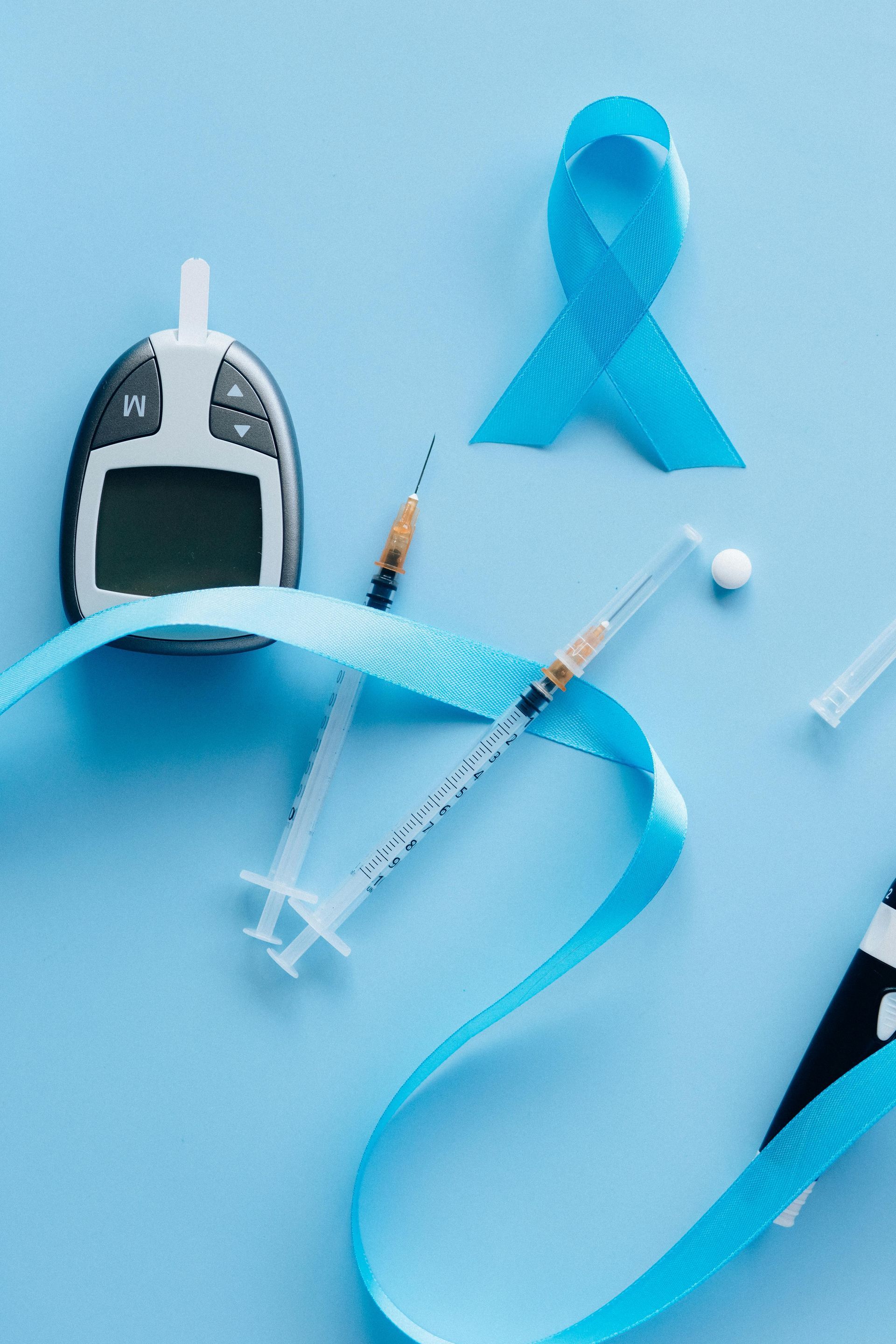 A blue ribbon , a syringe , a glucose meter and a needle on a blue background.