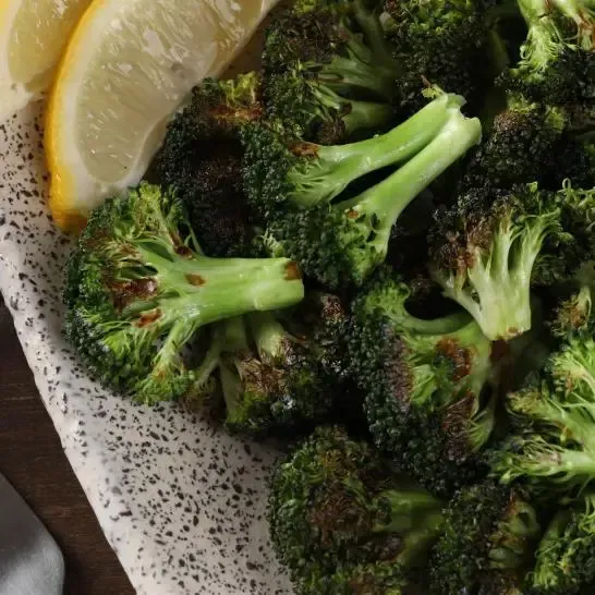 A plate of broccoli with lemon slices on a table.