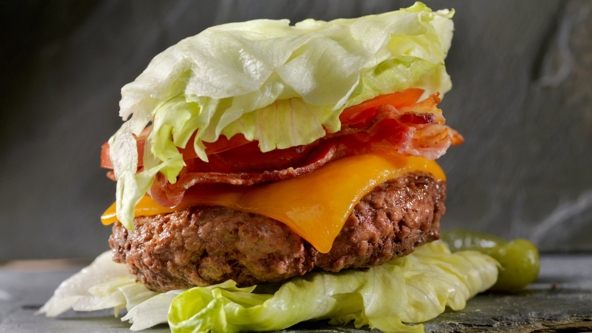 A close up of a hamburger with lettuce , cheese , tomatoes and bacon on a table.