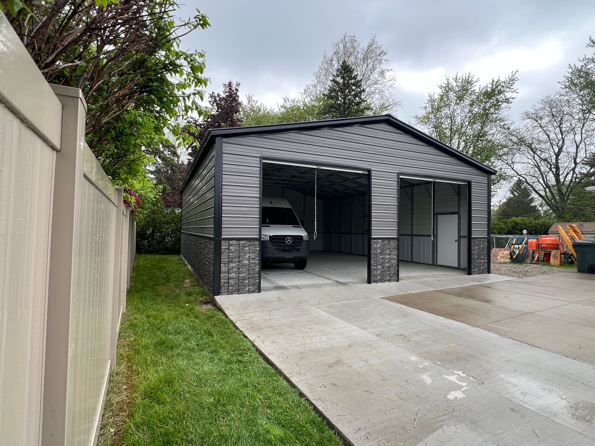 A green and white garage with two garage doors is sitting in the middle of a field.