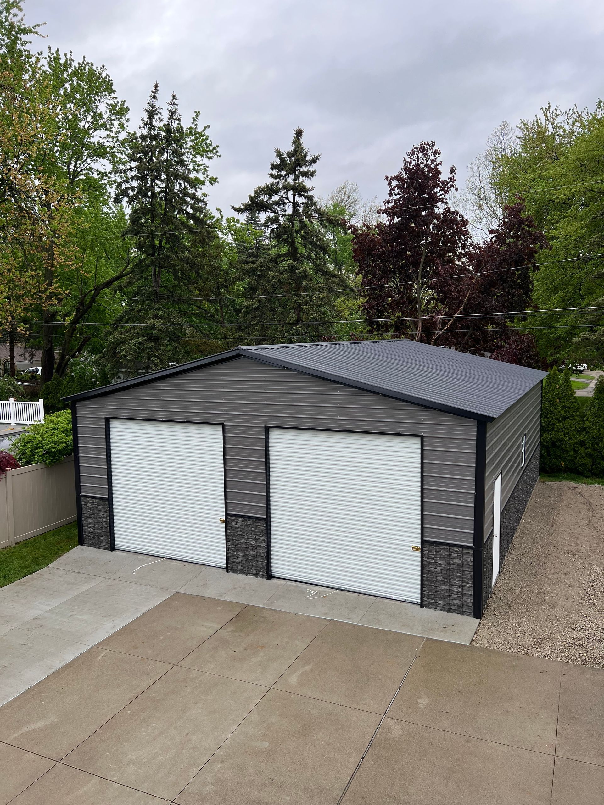 A white garage with a black roof is sitting next to a white house.