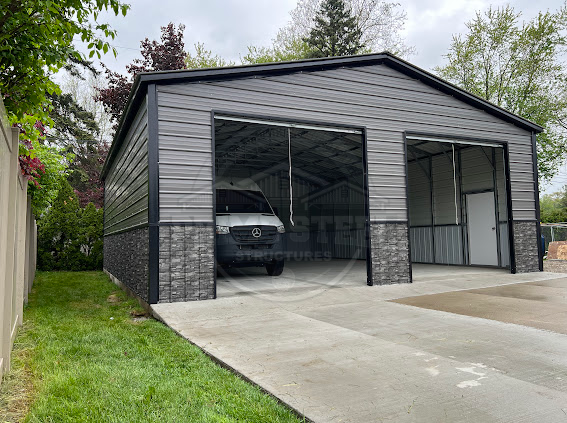 A green and white garage with two garage doors is sitting in the middle of a field.