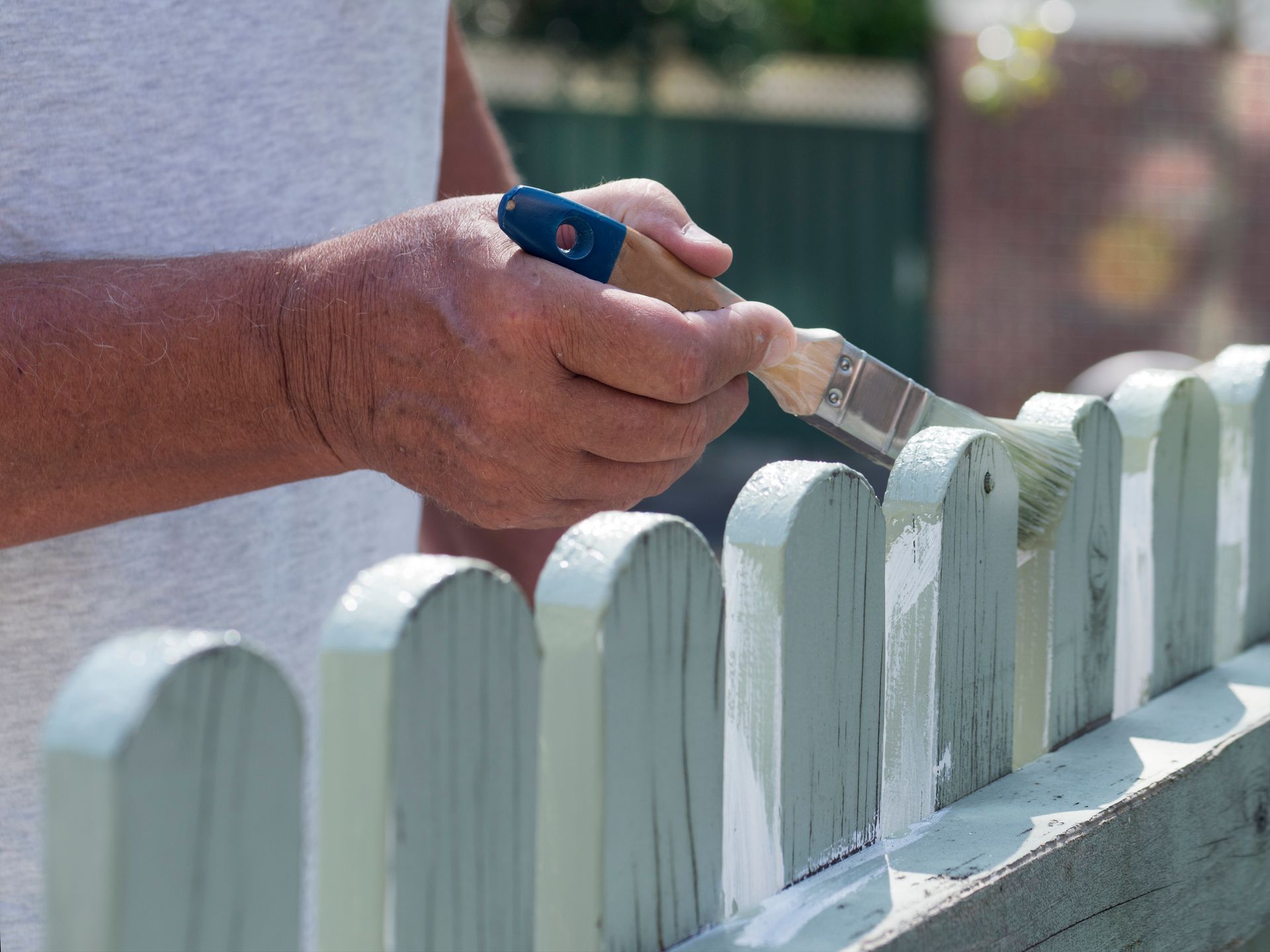 A man is painting a wooden fence with a brush.
