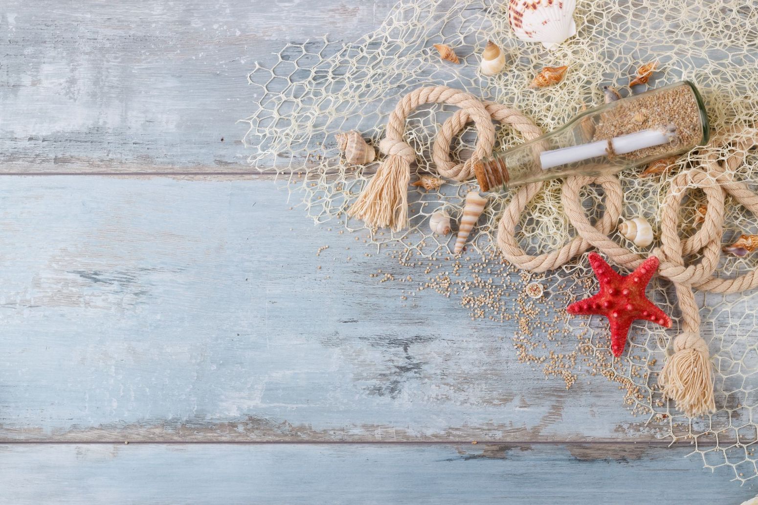 A wooden table topped with seashells , rope , starfish and a bottle with a message in it.