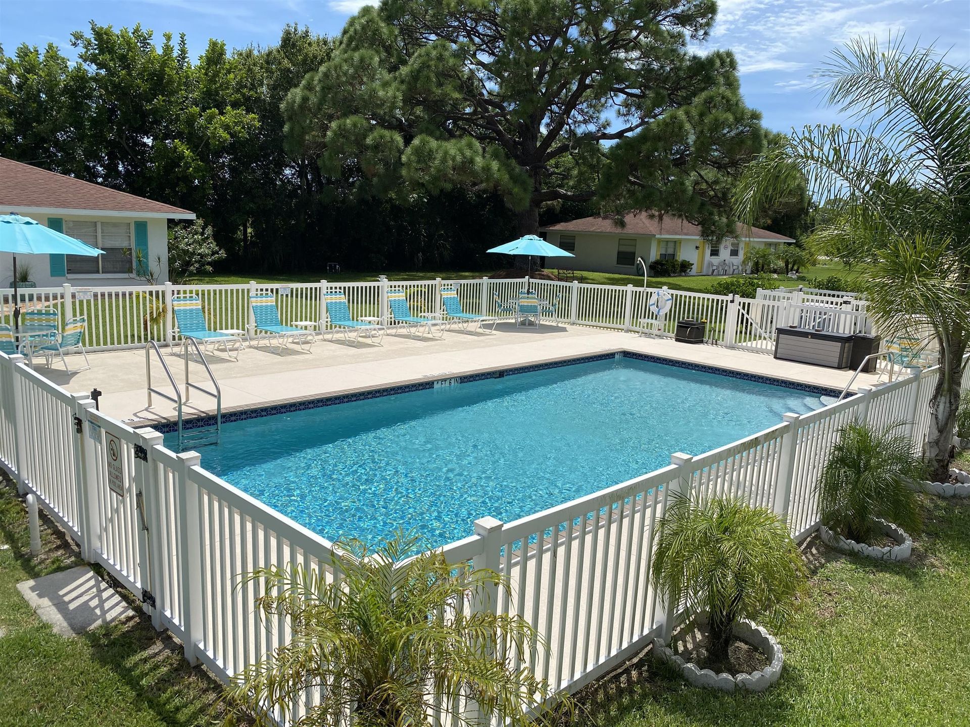 A large swimming pool surrounded by a white fence and chairs.