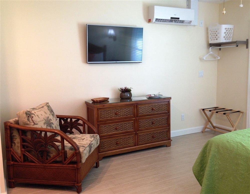 A bedroom with a chair a dresser and a flat screen tv