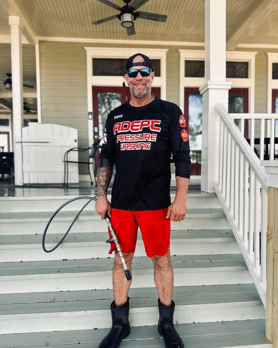 A person in a black long-sleeve shirt and red shorts holding a pressure washer wand while standing on a porch.
