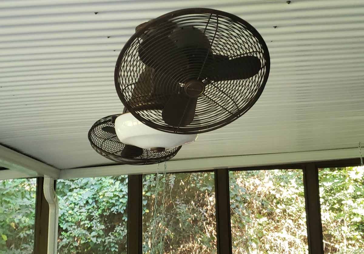Two fans are hanging from the ceiling of a screened in porch