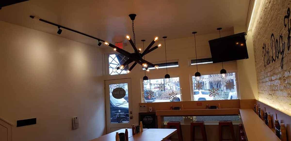 A restaurant with a long table and stools and a chandelier hanging from the ceiling.