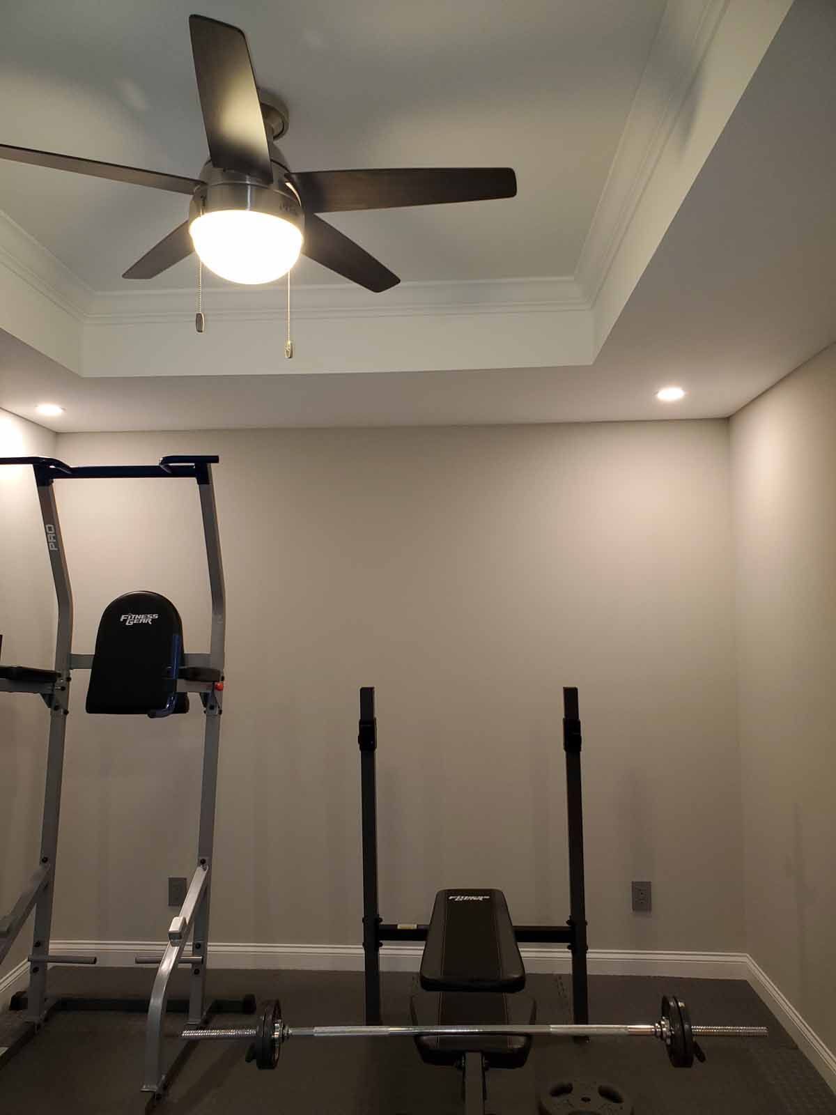 A gym with a ceiling fan and a bench.