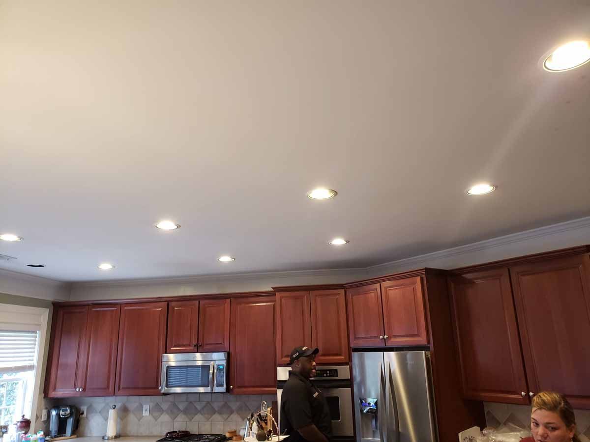 A man and a woman are standing in a kitchen with wooden cabinets and stainless steel appliances.