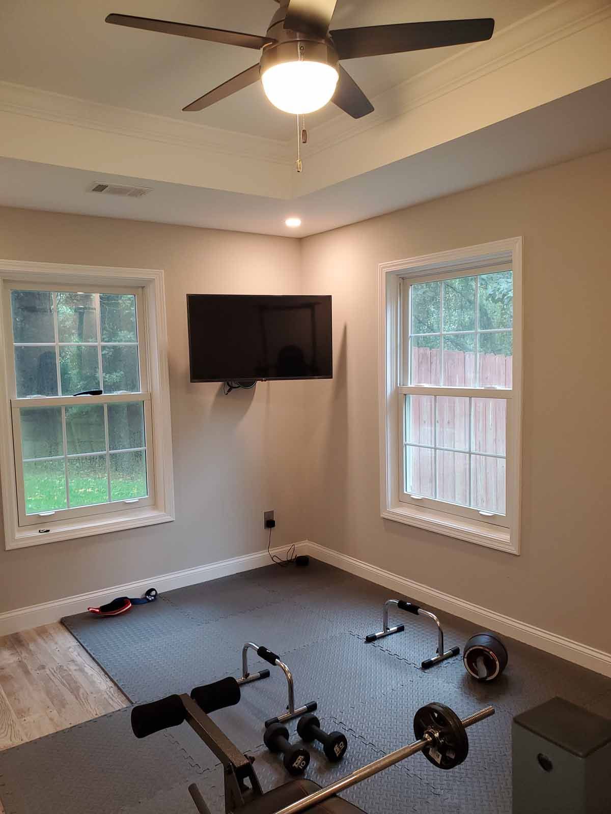 A room with a ceiling fan and a flat screen tv on the wall.