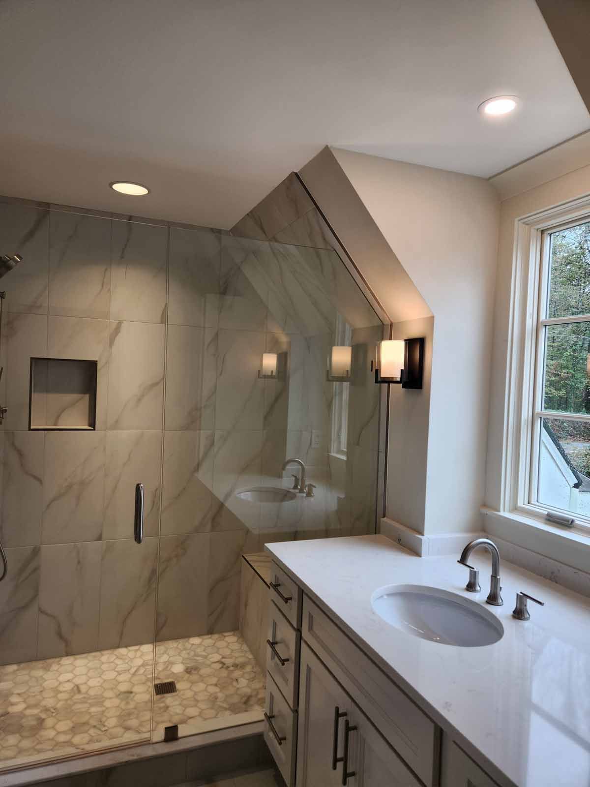 A bathroom with a sink , shower , mirror and window.