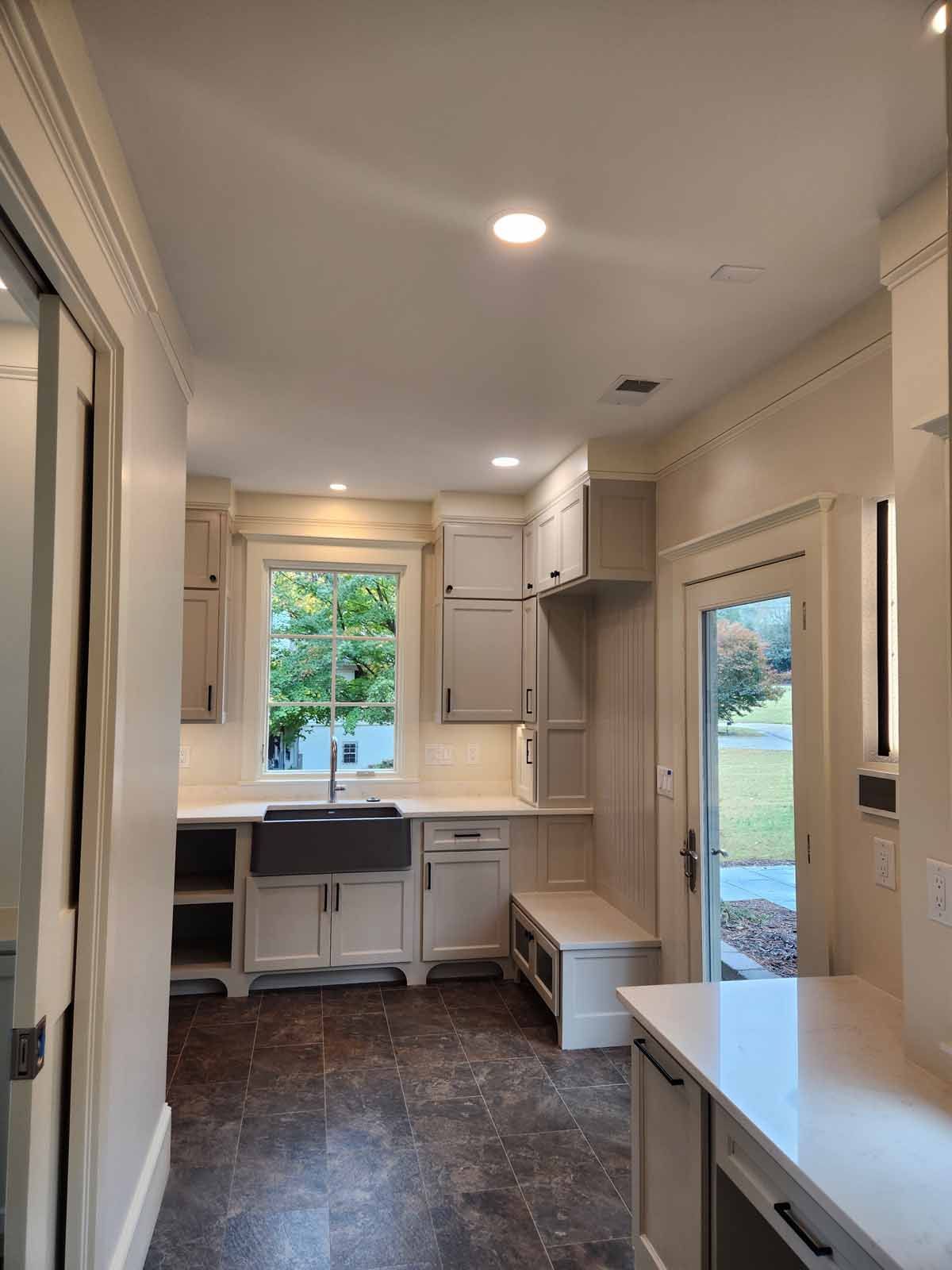 A kitchen with white cabinets , a sink , and a window.