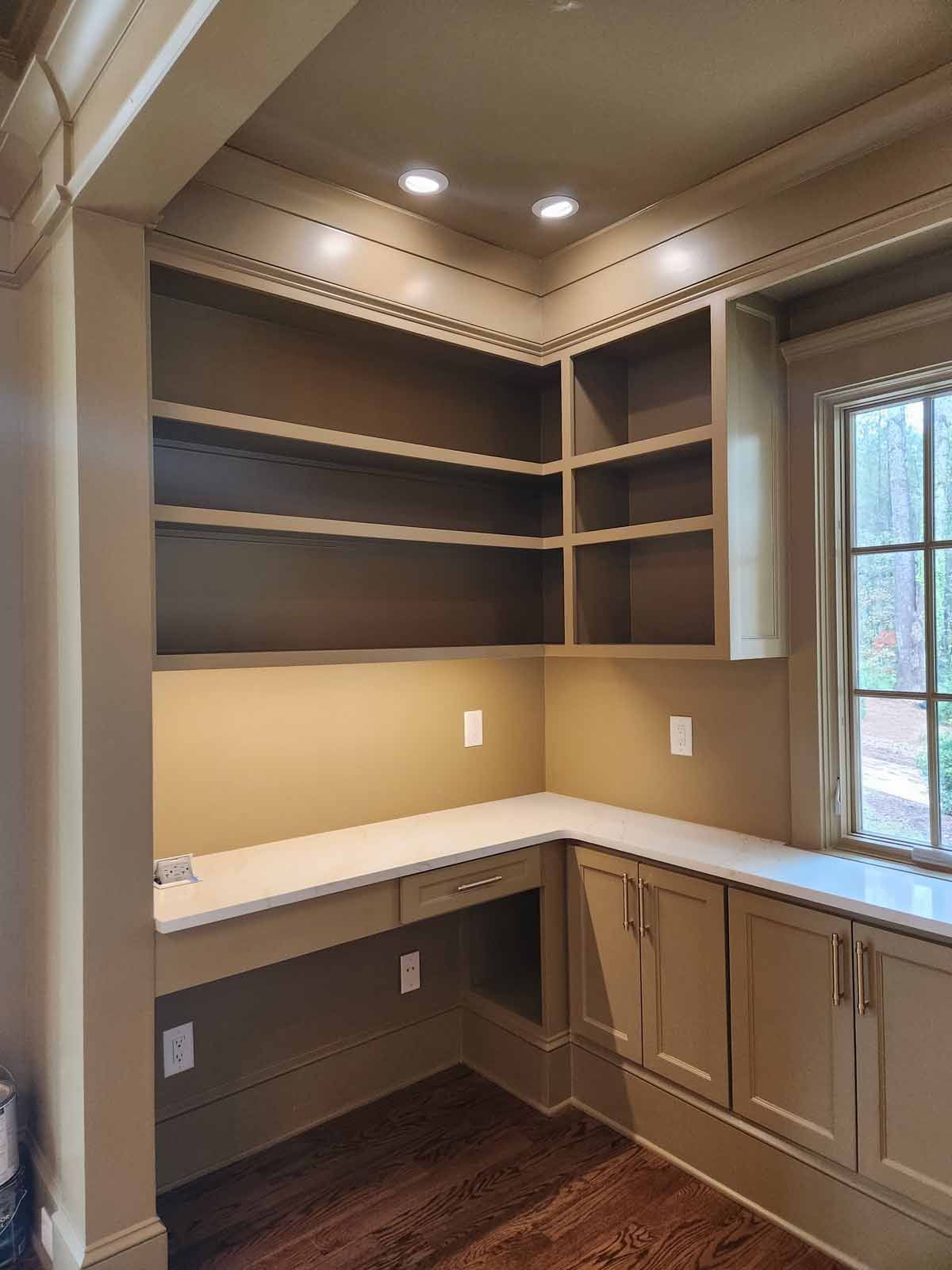 A room with a desk , cabinets , shelves and a window.