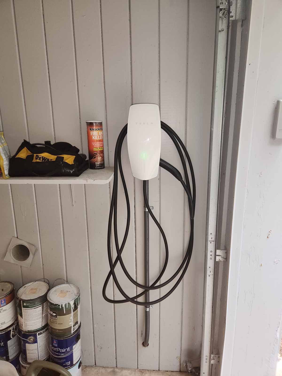 A tesla charging station is hanging on a wall in a garage.