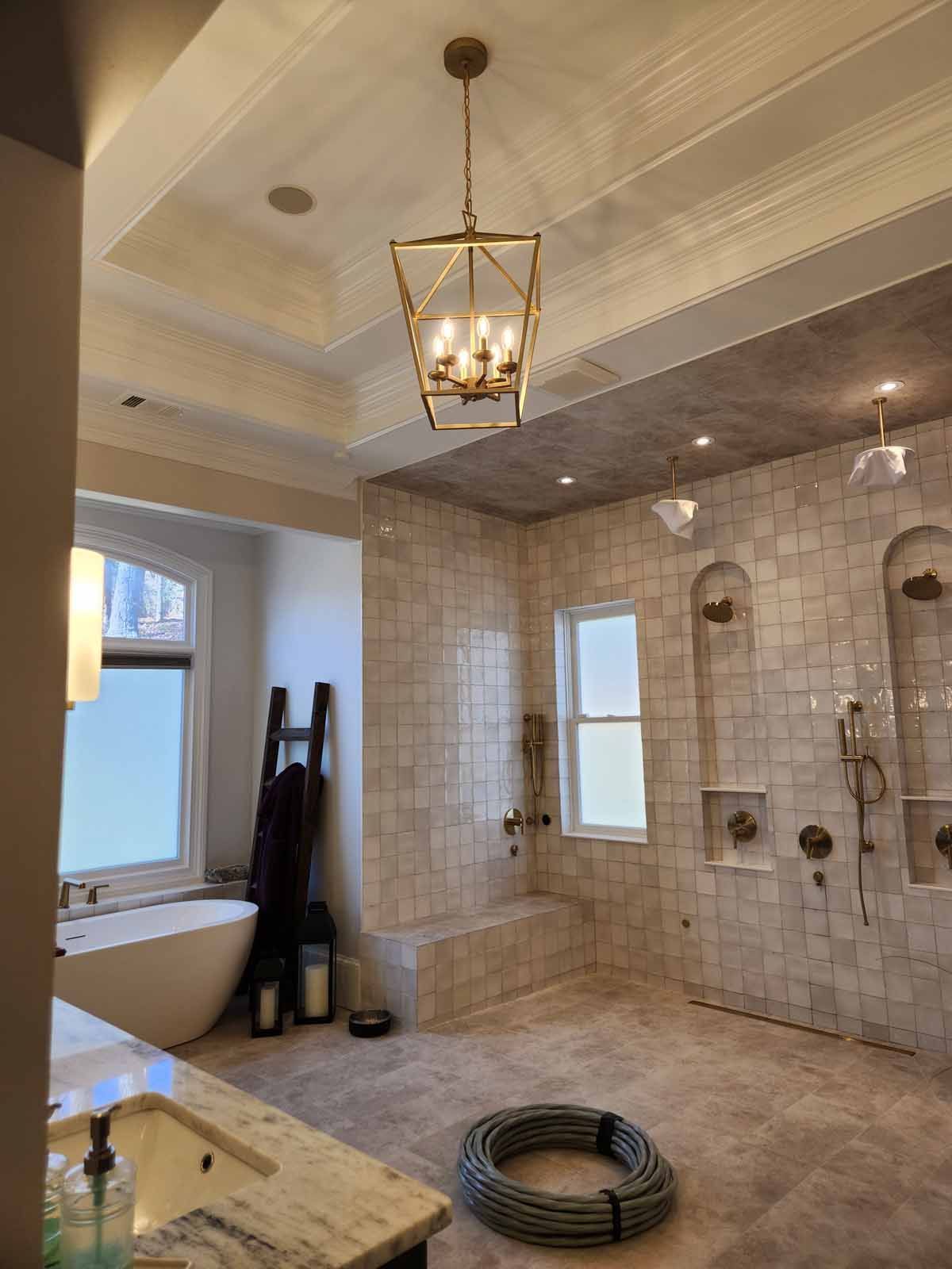 A bathroom with a tub , sink , shower and chandelier.