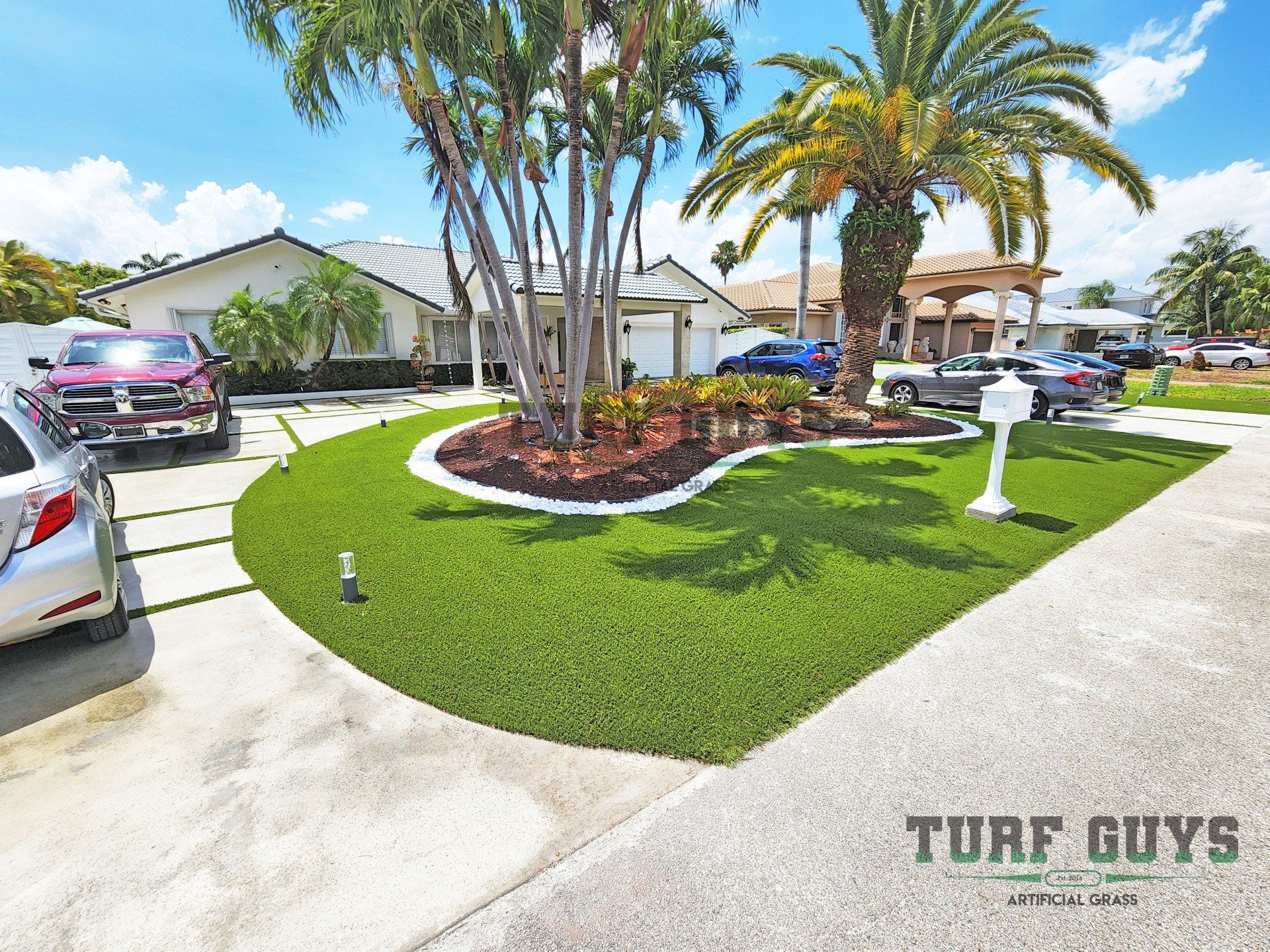 A green artificial lawn in front of a white house with palm trees and a white mailbox.