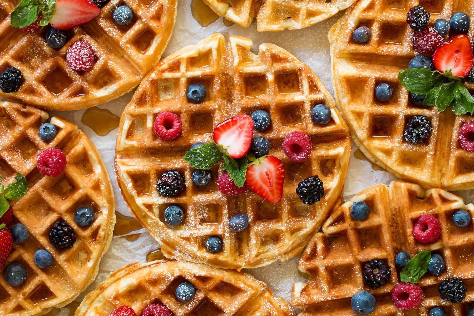 A close up of waffles with berries and syrup on a table.