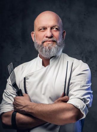 A bald man with a beard is holding a spatula and fork.