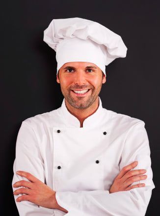 A smiling chef is standing with his arms crossed in front of a blackboard.