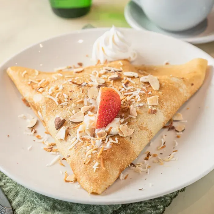 A close up of a crepe with whipped cream and strawberries on a plate.