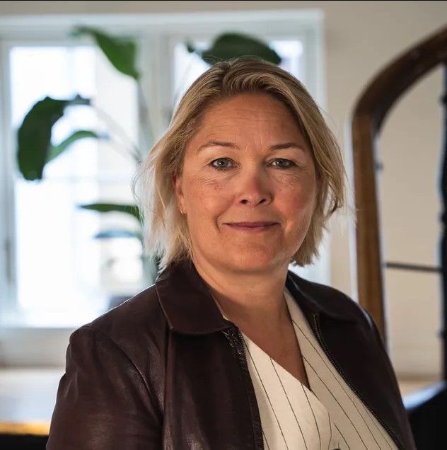 Een vrouw die een bruin leren jack draagt, lacht naar de camera