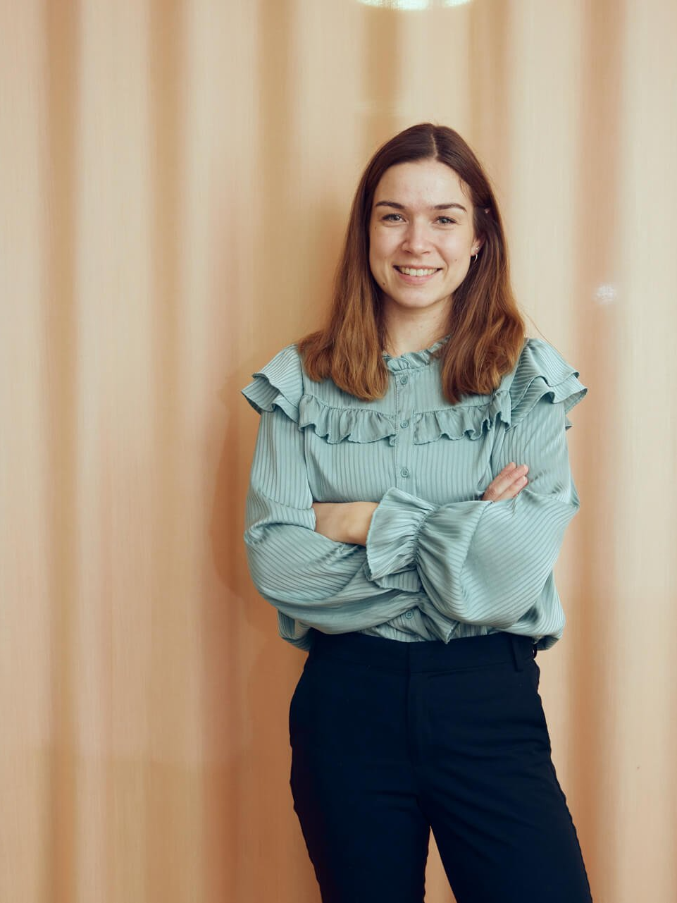 Een vrouw in een groene blouse en een zwarte broek staat met haar armen over elkaar.