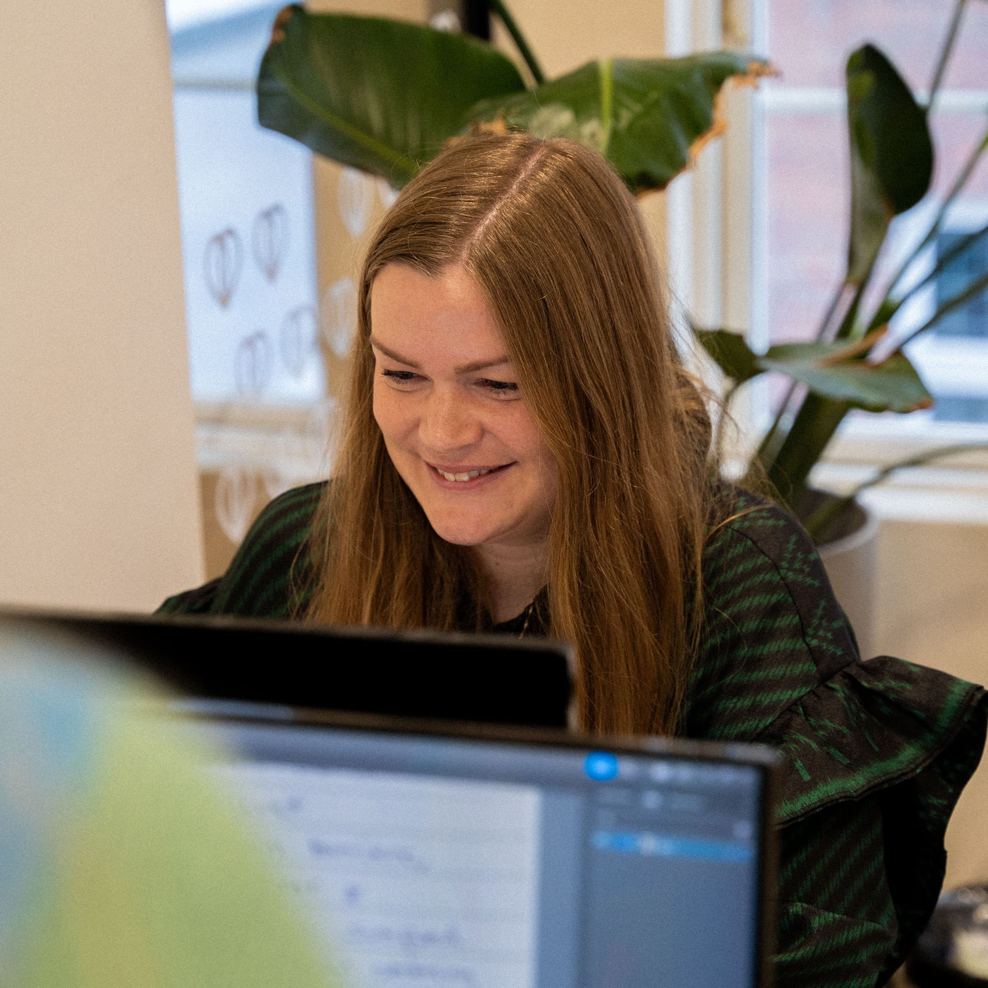 Een vrouw glimlacht terwijl ze naar een computerscherm kijkt.