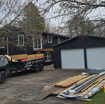 Three workers on a roof covered in bright blue underlayment, with ladders positioned against the siding of the house.