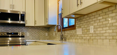 Three workers on a roof covered in bright blue underlayment, with ladders positioned against the siding of the house.