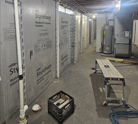 Three workers on a roof covered in bright blue underlayment, with ladders positioned against the siding of the house.