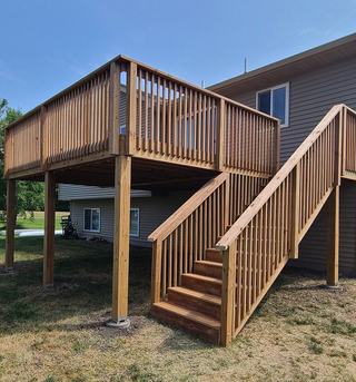 Three workers on a roof covered in bright blue underlayment, with ladders positioned against the siding of the house.