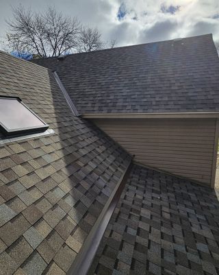 Three workers on a roof covered in bright blue underlayment, with ladders positioned against the siding of the house.