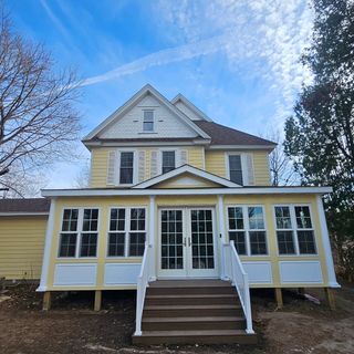 Three workers on a roof covered in bright blue underlayment, with ladders positioned against the siding of the house.