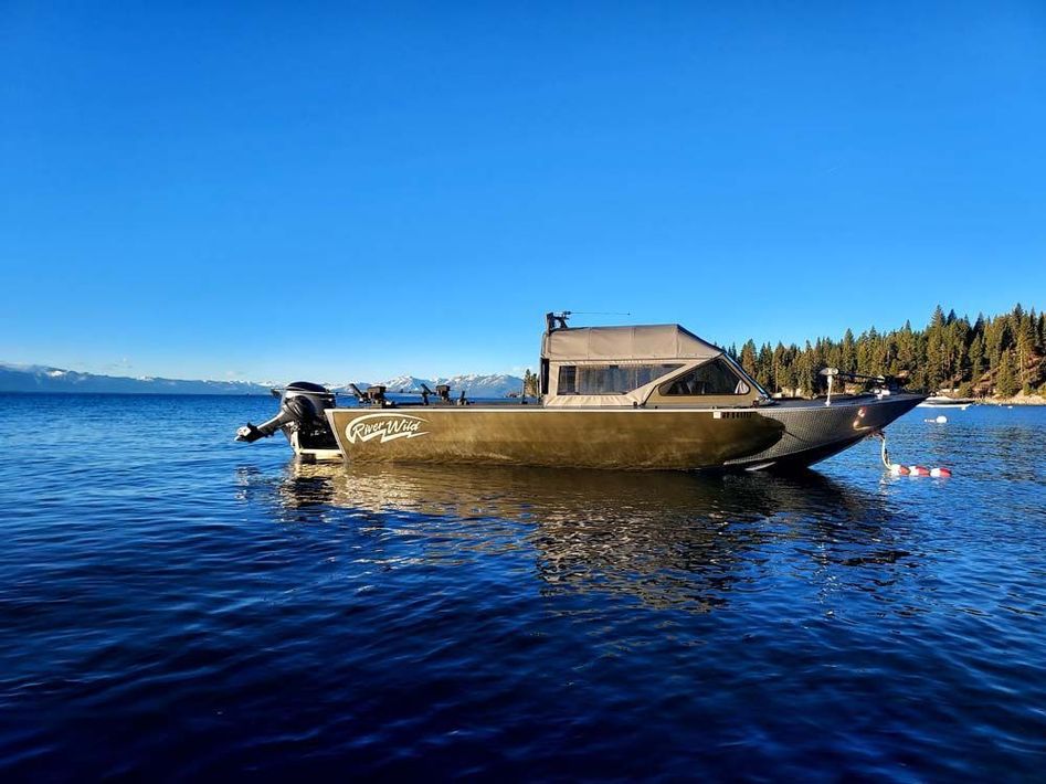 Olive-green motorboat on water, with mountains in background under clear blue sky.