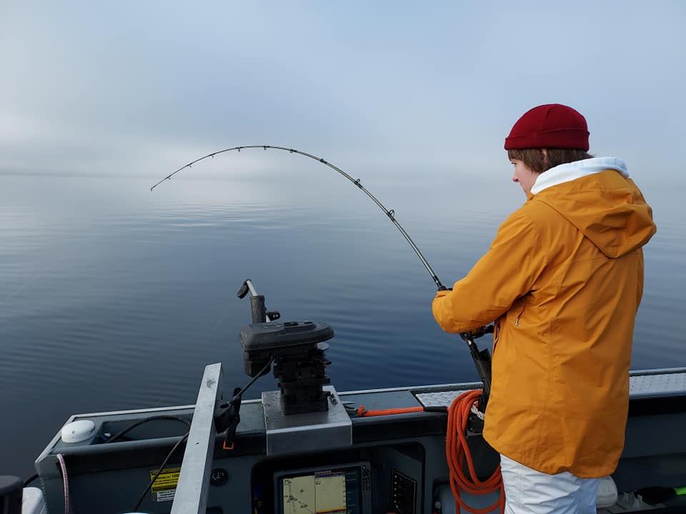 Person fishing on a boat, holding a bent fishing rod over calm water.