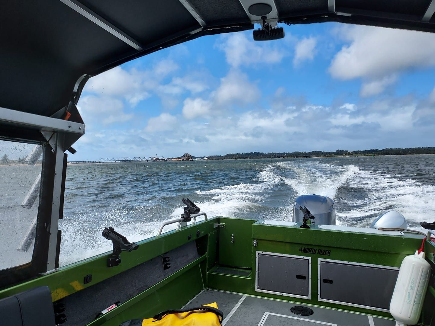 Green motorboat on choppy water, leaving a white wake, with a cloudy blue sky.